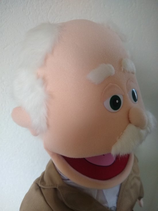 Poppenhoofd met glimlachend gezicht, witte haren, groene ogen en een bruin jasje.