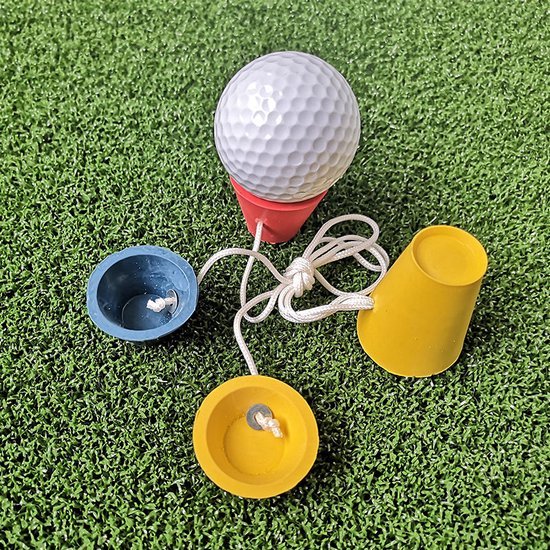 Golfbal op een rode tee, omringd door losse blauwe en gele tees, op groen kunstgras.