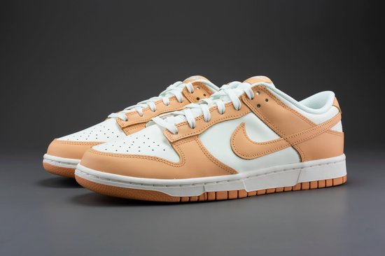 Een paar Nike Dunk Low damesschoenen, wit met oranje overlays, op een grijze achtergrond.