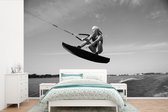 Behang - Fotobehang Een sportieve vrouw gaat laag door haar knieën op een wakeboard - zwart wit - Breedte 600 cm x hoogte 400 cm