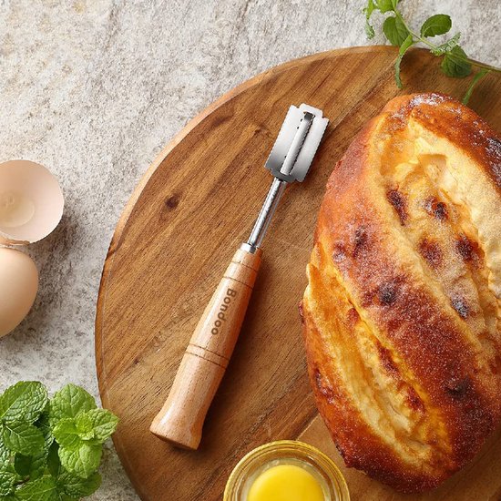 Deegmes met houten handvat ligt op een houten plank naast een versgebakken, goudbruin brood.