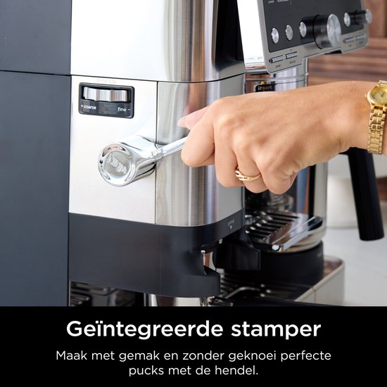 Hand met een ring draait de hendel van de ingebouwde tamper van de zilverkleurige Ninja koffiemachine.