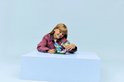 Une fille sourit en regardant un colibri LEGO et une fleur bleue qu'elle tient.