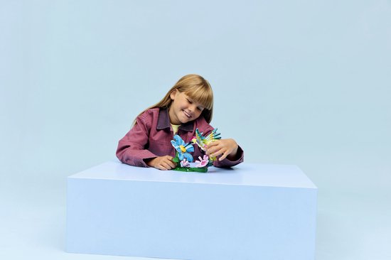 Une fille sourit en regardant un colibri LEGO et une fleur bleue qu'elle tient.