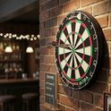 Een dartbord met de traditionele kleuren groen, rood en zwart, met twee pijltjes erin. Hangt aan een bakstenen muur.