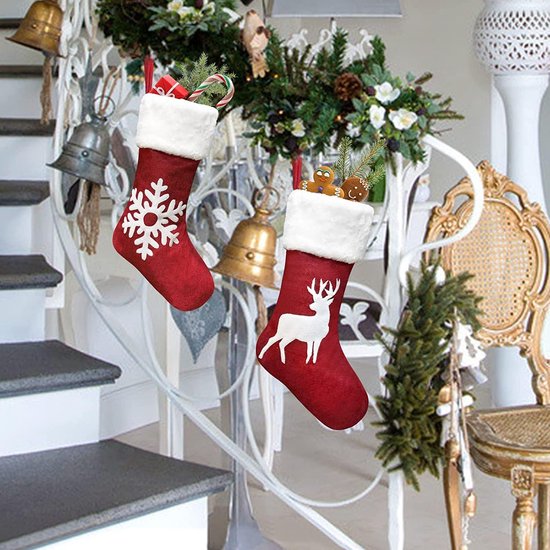 Deux chaussettes de Noël rouges à bordure blanche, l'une avec un flocon de neige, l'autre avec un cerf. Suspendues à une rampe d'escalier.