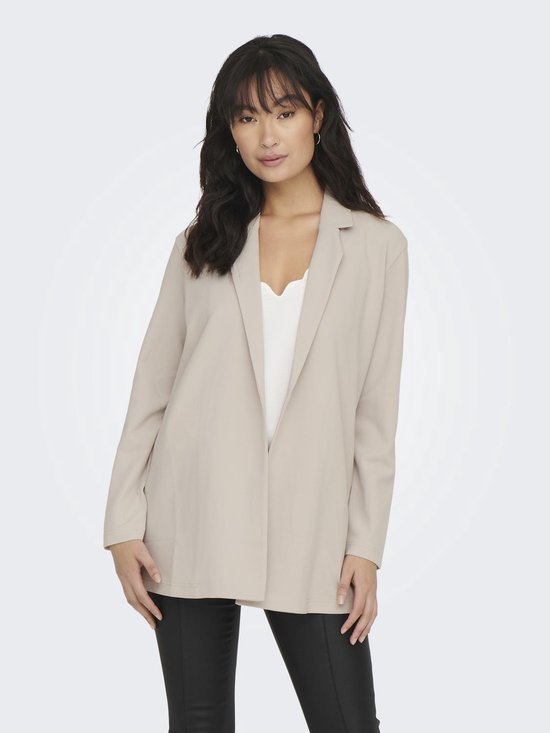 Vrouw met lange, golvende donkere haren in een lange, beige blazer met open voorkant en een witte top.