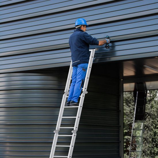 Man met helm op ladder monteert gevelbeplating met boormachine.