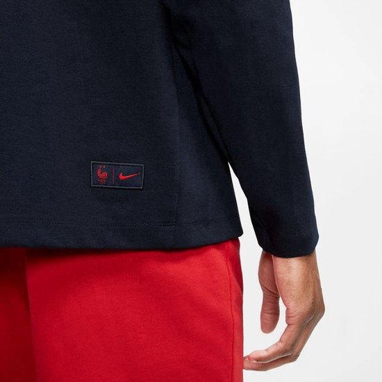 Detail van de mouw van een donkerblauw Nike Tech vest met rood embleem met haan en Nike logo.
