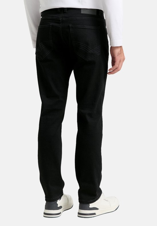 Man in zwarte jeans met een witte longsleeve, staand van achteren.
