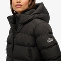 Zwarte gewatteerde jas met capuchon. Close-up van de linker mouw met Superdry-logo-badge.