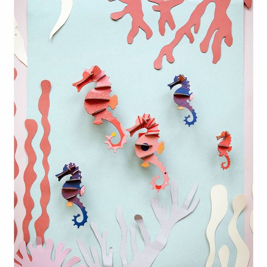 Vier kartonnen zeepaardjes, roze en blauw, met patronen, te midden van koraal en zeewier.