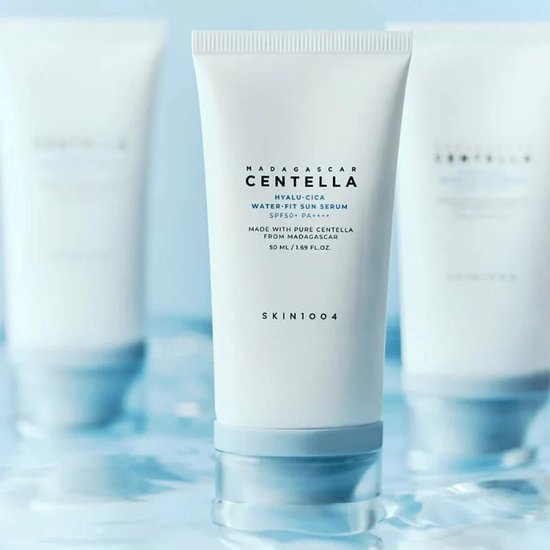 Drie witte tubes Centella Hyalu-Cica Water Fit Sun Serum op een waterachtige blauwe achtergrond.