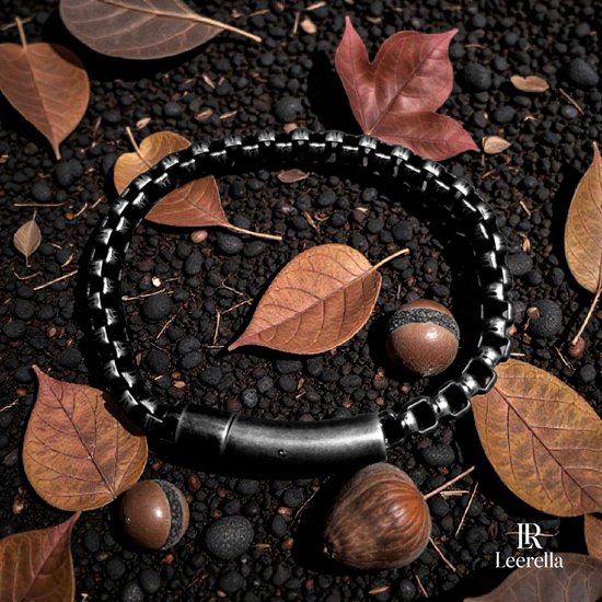 Donkergrijze roestvrijstalen schakelarmband op een bed van zwarte stenen, omringd door herfstbladeren en kastanjes.