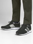 Man met zwarte lage sneakers met witte en grijze strepen, gedragen met een groene broek.