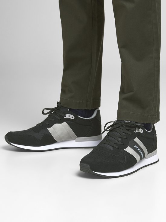 Man met zwarte lage sneakers met witte en grijze strepen, gedragen met een groene broek.