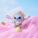 Een Stitch pluche speelgoedje in een beige slaapmutsje, met een kopje in de handen, zittend op een gele bol.