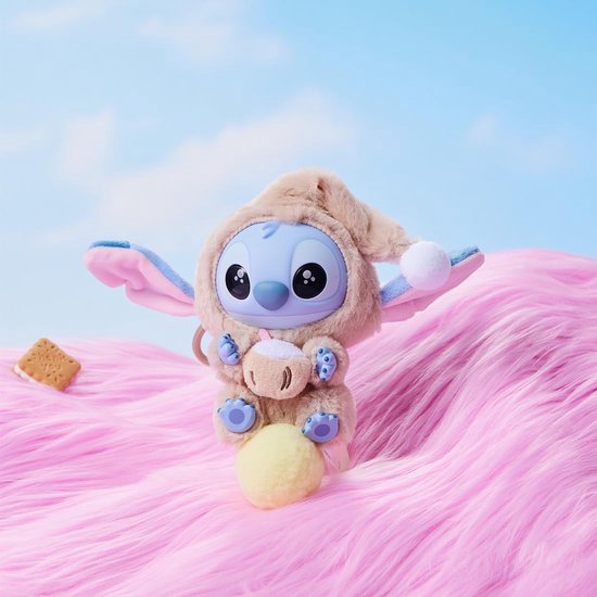 Een Stitch pluche speelgoedje in een beige slaapmutsje, met een kopje in de handen, zittend op een gele bol.