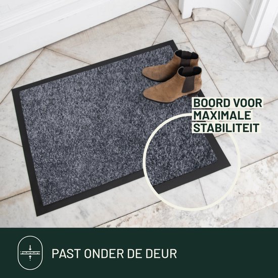 Grijze deurmat met zwarte rand, met twee bruine laarzen erop. Tekst 'Boord voor maximale stabiliteit'.