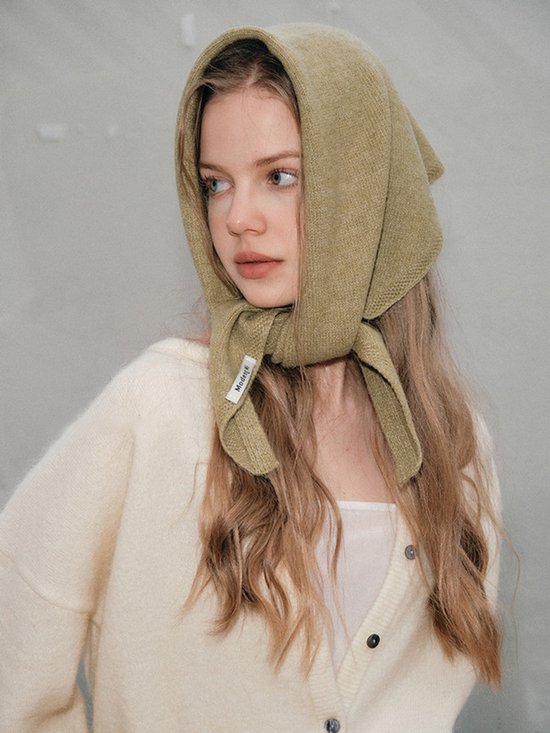 Model draagt een gebreide gebroken witte vest. De olijfgroene sjaal wordt als hoofddoek gedragen met de uiteinden geknoopt.
