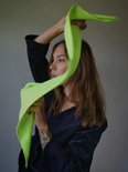 Vrouw met tatoeages houdt een felgroene gebreide sjaal omhoog bij haar hoofd.