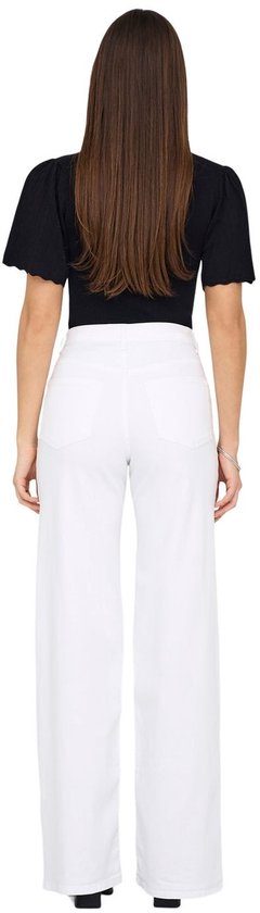 Vrouw met lange bruine haren in zwarte top en witte wide-leg jeans, van achteren gezien.