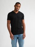 Man met donkere huid, met kort zwart V-hals T-shirt en lichtblauwe jeans.