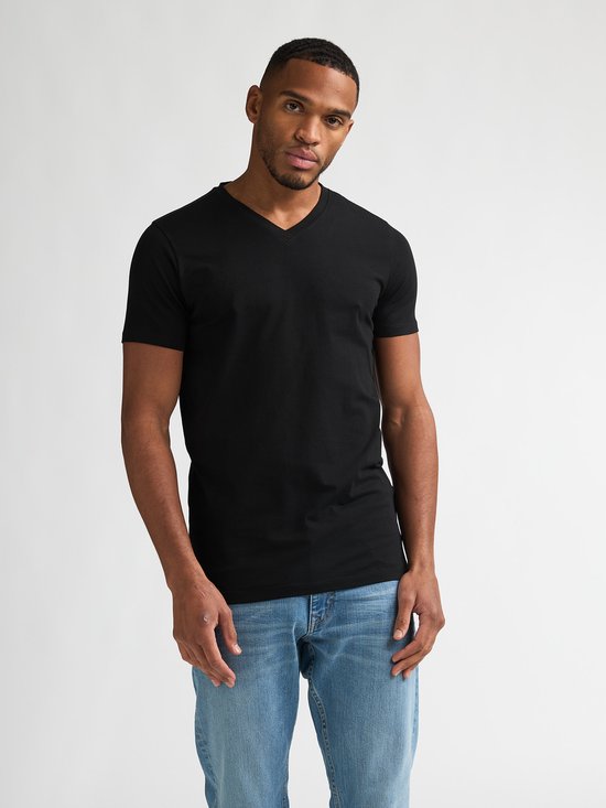 Man met donkere huid, met kort zwart V-hals T-shirt en lichtblauwe jeans.