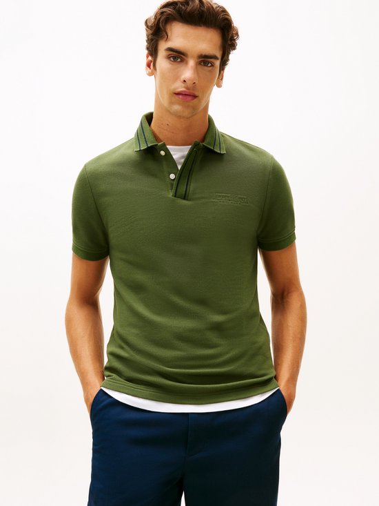 Model draagt een donkergroen poloshirt met korte mouwen, geborduurd logo op borst en contrasterende streep op kraag.