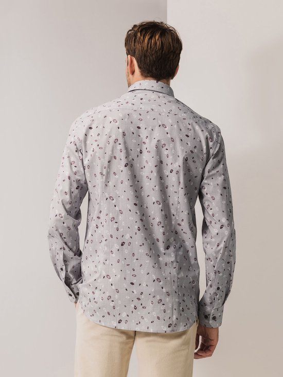 Man van achteren met een grijs overhemd met bloemenprint en beige broek.