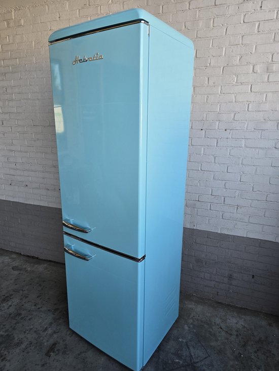 Hemelsblauwe Helvetia koelkast met zilveren handgrepen, staand tegen een witte bakstenen muur.