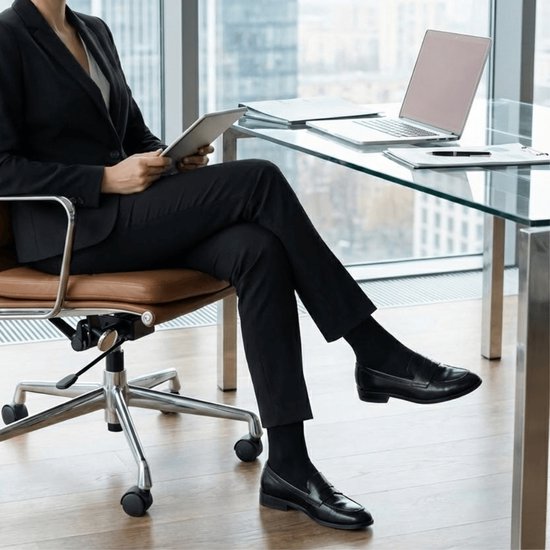 Zakelijke outfit: persoon in zwart pak en zwarte sokken zittend aan een glazen bureau.