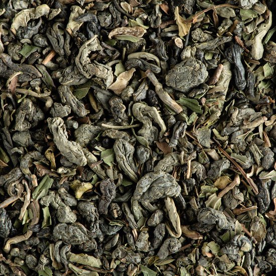 Gedroogde groene thee met stukjes munt. Losse thee, donkergroene en bruine blaadjes met steeltjes.
