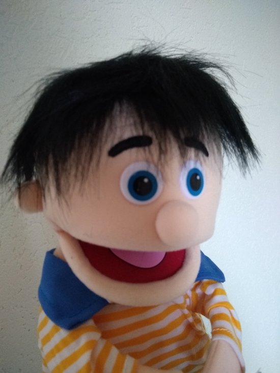 Close-up van handpop Bobbie met zwart pluizig haar, blauwe ogen, een gele-oranje gestreepte trui en een blauwe kraag.