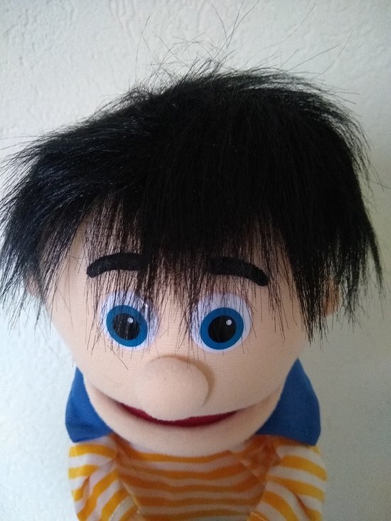 Close-up van een handpop met zwart pluizig haar, blauwe ogen en een geel-oranje gestreepte trui.