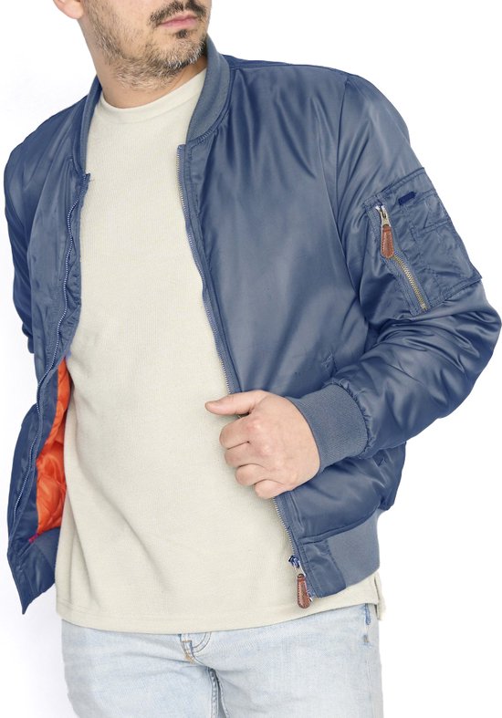 Man met blauwe bomberjack met oranje binnenvoering, open ritssluiting, beige T-shirt en spijkerbroek.