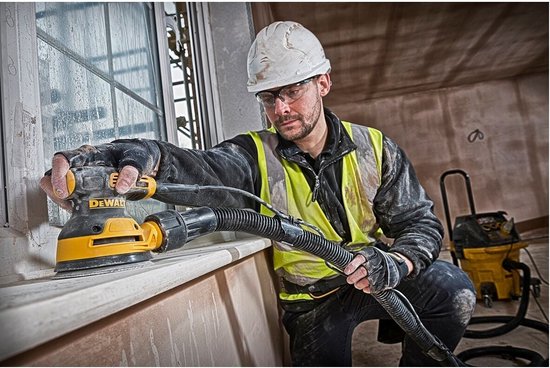 Man in veiligheidsuitrusting schuurt een vensterbank met een gele en zwarte DeWalt schuurmachine.