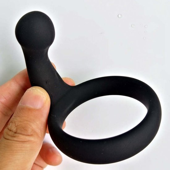 Een hand houdt een zwarte, flexibele penisring met een bolletje aan het uiteinde vast.