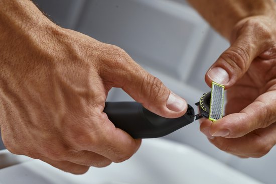 Handen verwisselen het mesje van een zwart met groen Philips OneBlade scheerapparaat.