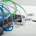 Een zwart laadstation met USB, Laptop en Phone labels op de kabels.