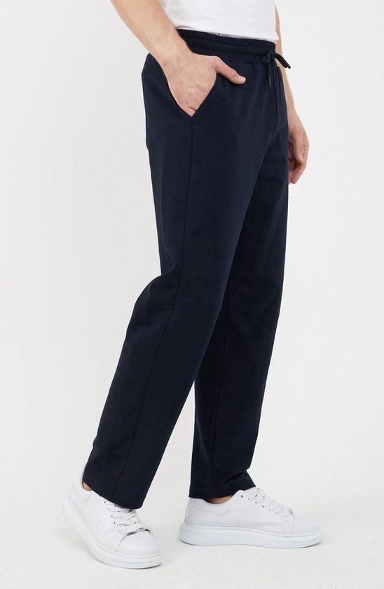 Donkerblauwe joggingbroek met trekkoord, gedragen door een man met een wit T-shirt en witte sneakers, vanuit de zijkant gezien.