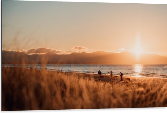 WallClassics - Dibond - Zon Verdwijnend achter Bergen bij Strand - 105x70 cm Foto op Aluminium (Wanddecoratie van metaal)