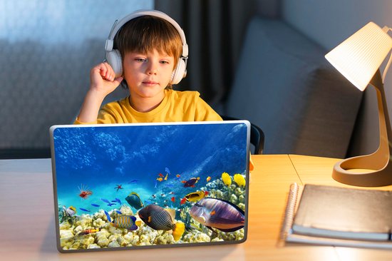 Ordinateur portable avec autocollant monde sous-marin : coraux, poissons et poisson-lion, près d'un garçon avec casque.