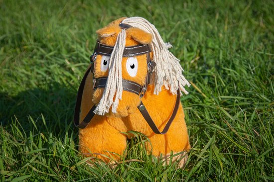 Oranje knuffelpony met bruine leren hoofdstel en witte manen, zittend in gras.