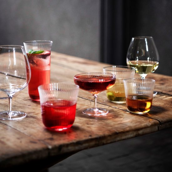 Verschillende glazen met drankjes op een houten tafel, waaronder geribbelde glazen.