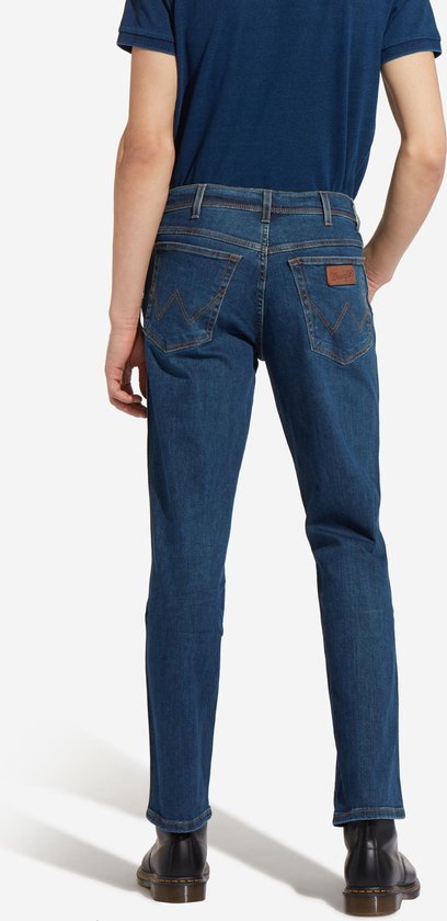 Blauwe Wrangler jeans, regular fit, gedragen met donkerblauw T-shirt en zwarte schoenen, van achteren gezien.