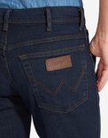 Close-up van de achterzak van een donkerblauwe Wrangler jeans met iconische stiksels en een bruine merkpatch.
