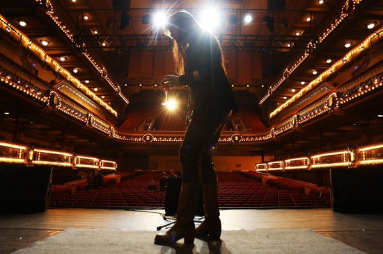 Silhouet van een vrouw op een podium voor een lege theaterzaal met veel lampjes.