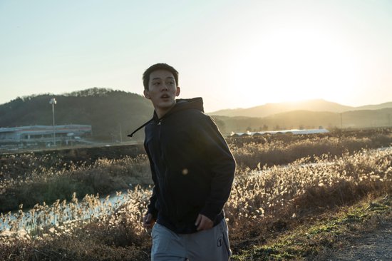 Een jonge man in een zwarte hoodie rent in een veld bij zonsondergang.