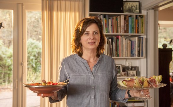 Vrouw in grijs gestreept shirt houdt twee schalen met hapjes vast in een woonkamer met boekenkast.